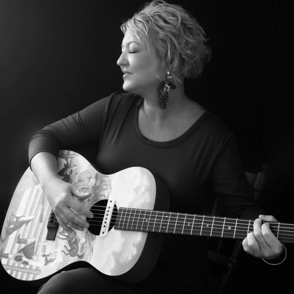 A black and white image of Stefani with eyes closed holding her guitar.